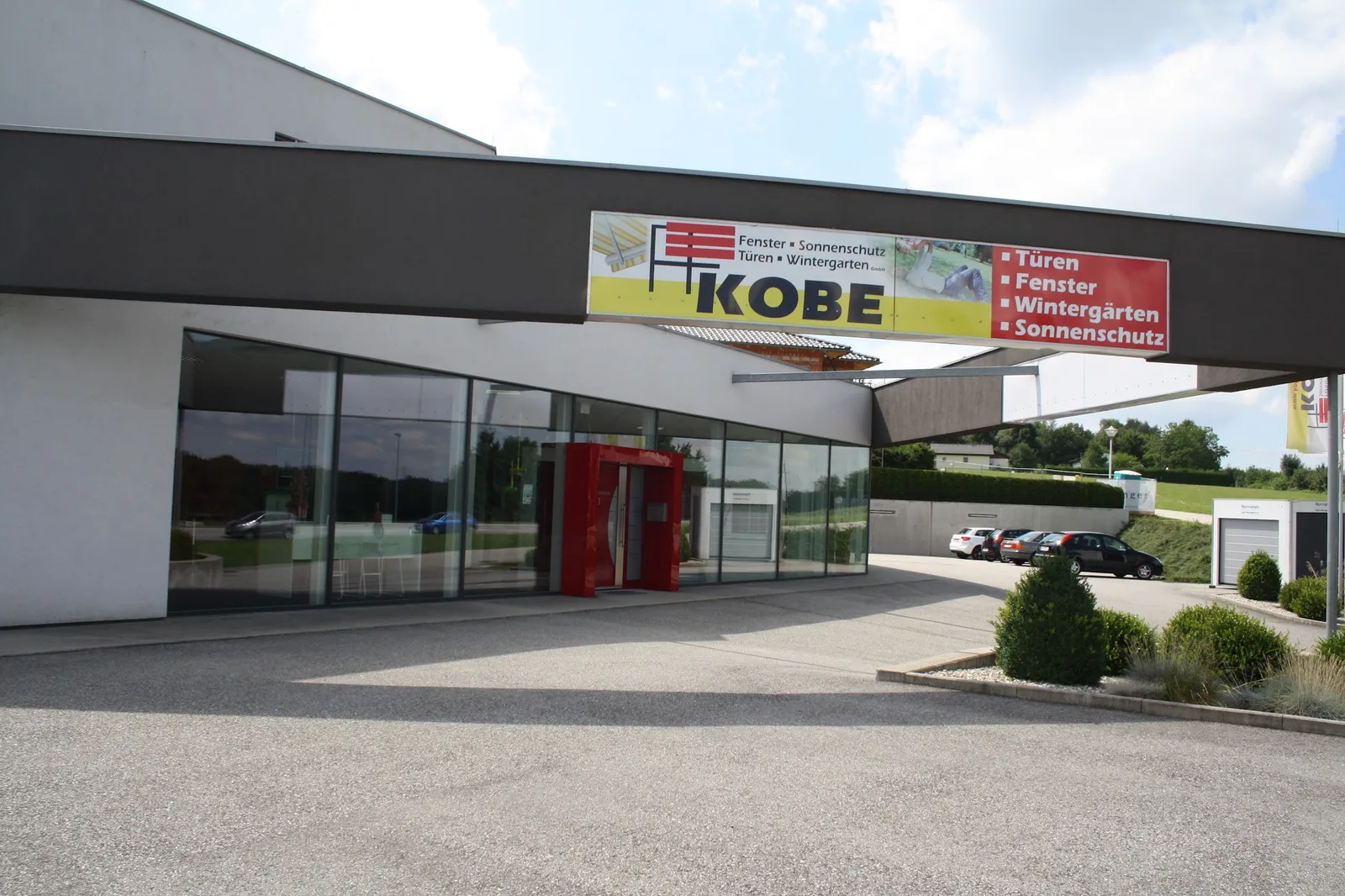 Ausstellung von KOBE in Hohenzell mit Glasfront, roter Eingangstür und Transparent