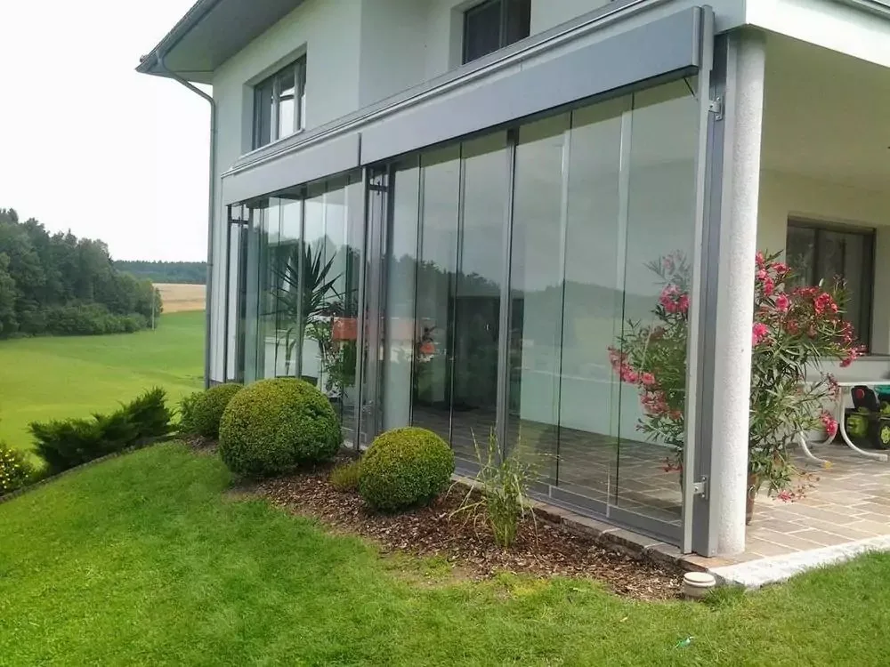 Großflächige Glasschiebewände an einem Wohnhaus, davor Rasen und Buchskugeln
