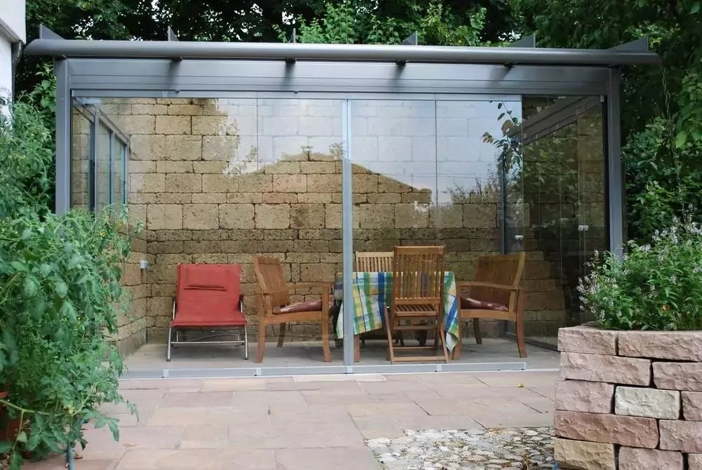 Glashaus vor einer Natursteinmauer mit roten Stühlen