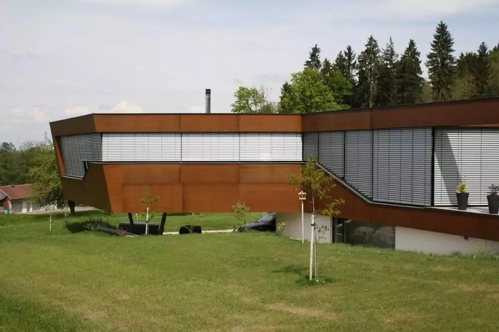 Moderner Bau mit rostbrauner Fassade und Raffstores auf einer Wiese