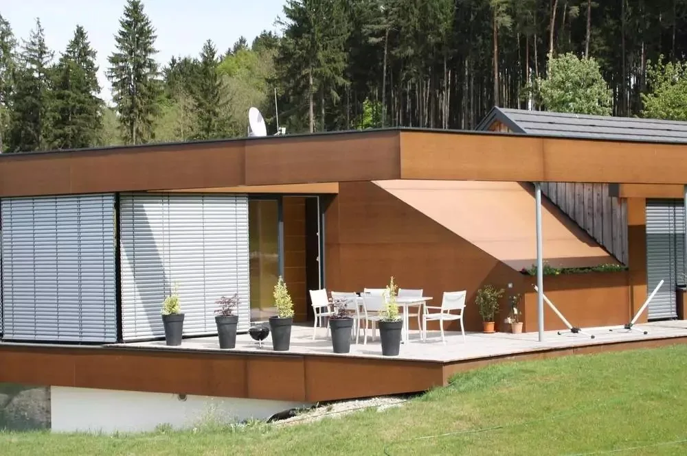 Flachdachhaus mit rostbrauner Fassade, Raffstores und Terrasse am Waldrand