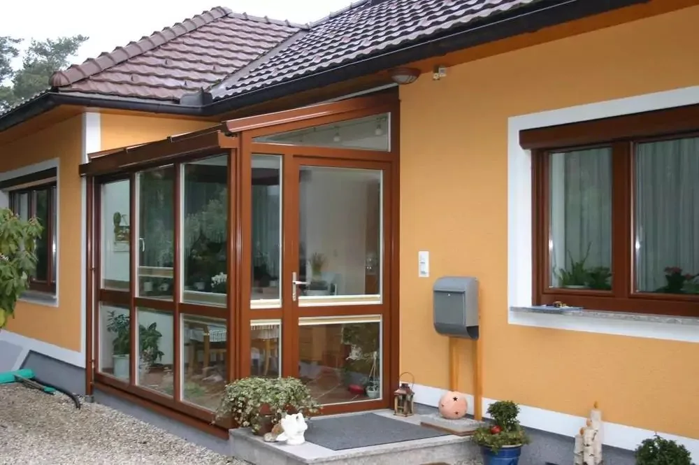 Holz-Wintergarten mit Sprossenfenstern an einem orangefarbenen Haus
