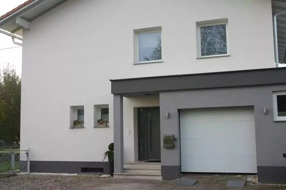 Hauseingang mit dunkler Haustür, Vordach und weißem Sektionaltor
