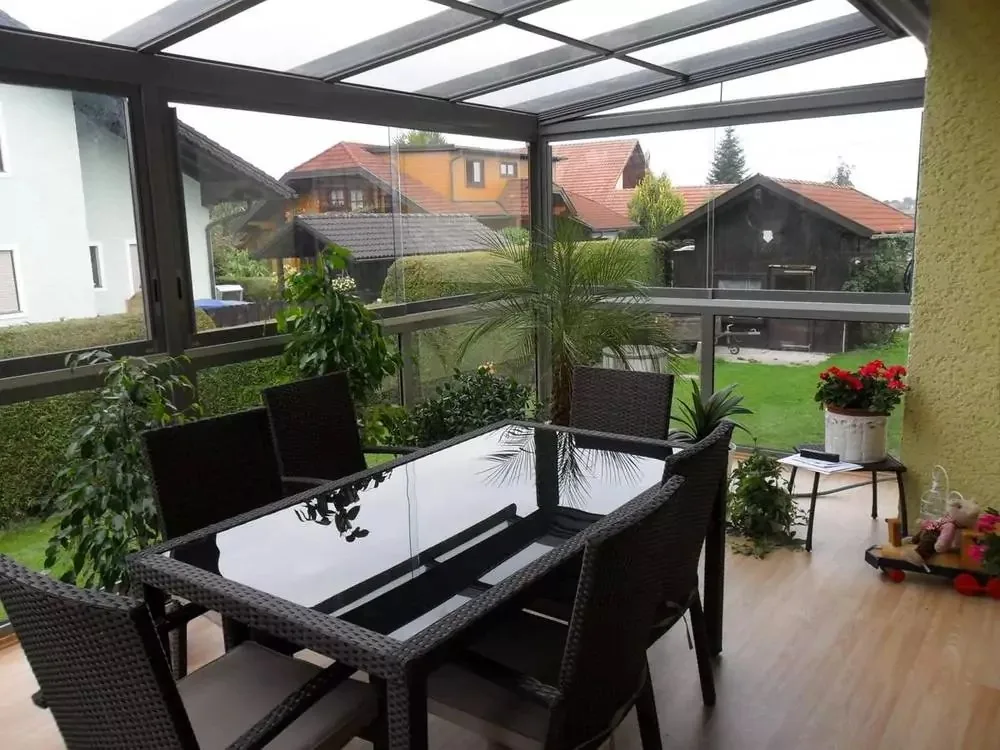 Terrassendach mit Glaswänden, darunter Esstisch und Stühle, Blick auf Nachbarhäuser